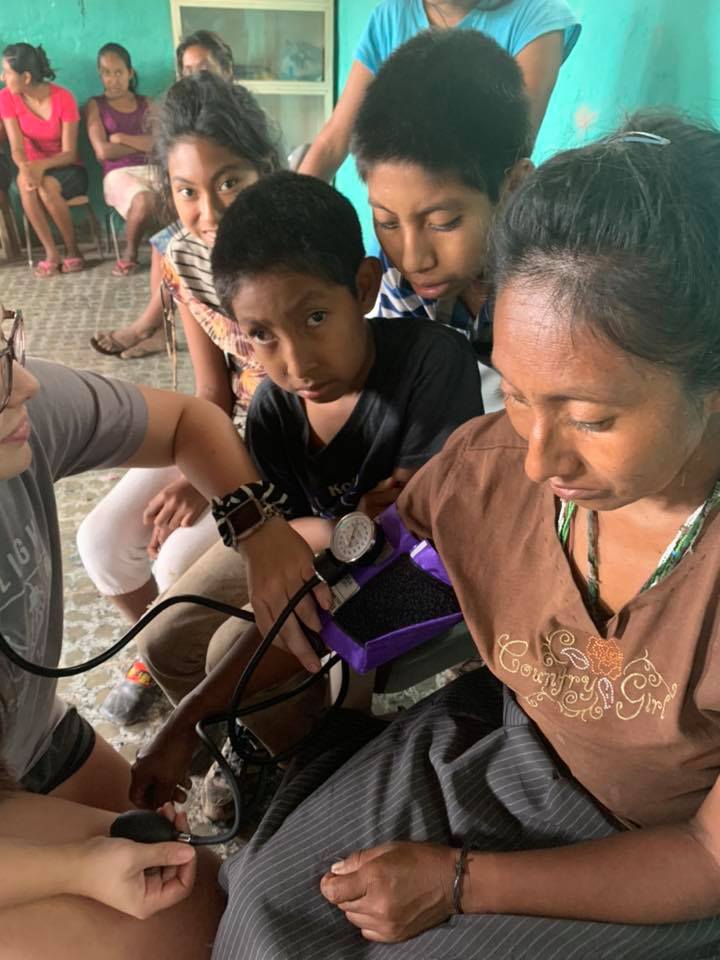nurse checking a woman's blood pressure while her children look on in a makeshift clinic in honduras